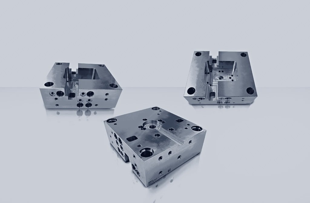 Drei CNC-bearbeitete Formgrundplatten mit Kavitäten, Aussparungen und Schraubenbohrungen aus unterschiedlichen Blickwinkeln.