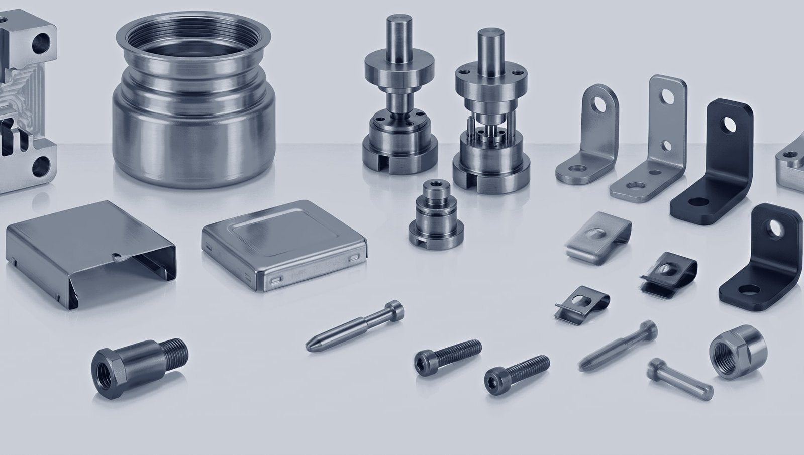 Eine breite Palette gefertigter und gestanzter Teile – eine große Gewindehülse aus Stahl, ventilartige Baugruppen, Blechgehäuse, Winkel, Clips, Schrauben und Bolzen.